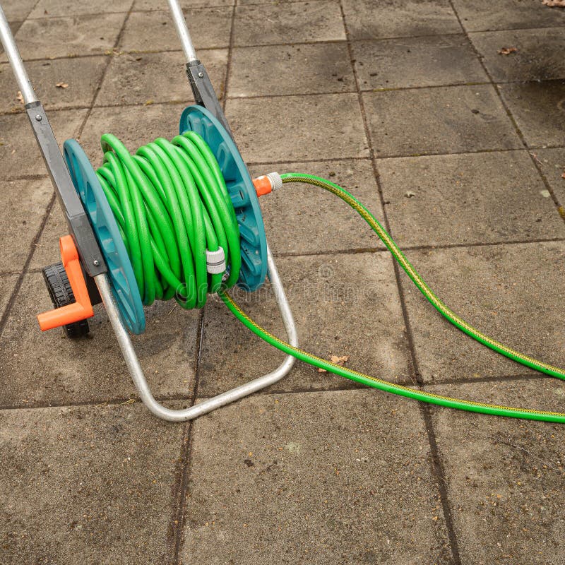 Una bobina di manichetta con un tubo verde in piedi sulle vecchie bramme di cemento sporche immagine stock