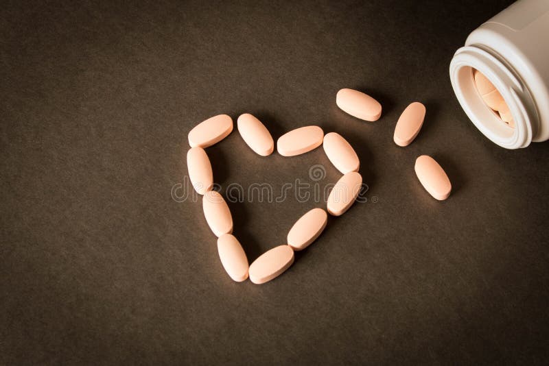 Una bottiglia aperta delle pillole su fondo scuro Pillole Heart-Shaped