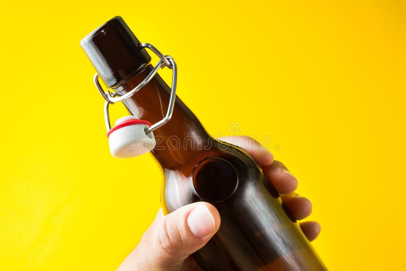Una bottiglia marrone con birra senza un'etichetta su un fondo giallo in sua mano immagini stock libere da diritti Una bottiglia marrone con birra senza un'etichetta su un fondo giallo in sua mano immagini stock libere da diritti
