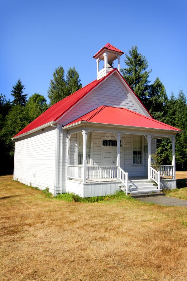 A typical white 1908 one room school house with a bell tower on the red metal roof. Trees and blue sky. A typical white 1908 one room school house with a bell tower on the red metal roof. Trees and blue sky.