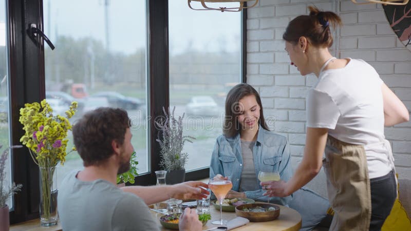 Una cameriera amichevole in un caffè accogliente ha portato da bere a una coppia piacevole. un uomo e una donna sono venuti a pran archivi video