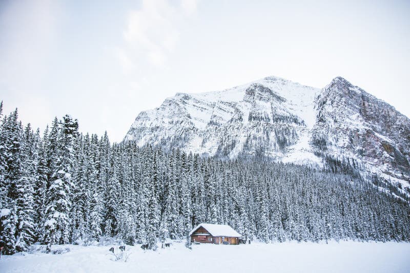 Una capanna in un campo nevoso con le montagne rocciose e una foresta fotografia stock libera da diritti Una capanna in un campo nevoso con le montagne rocciose e una foresta fotografia stock libera da diritti