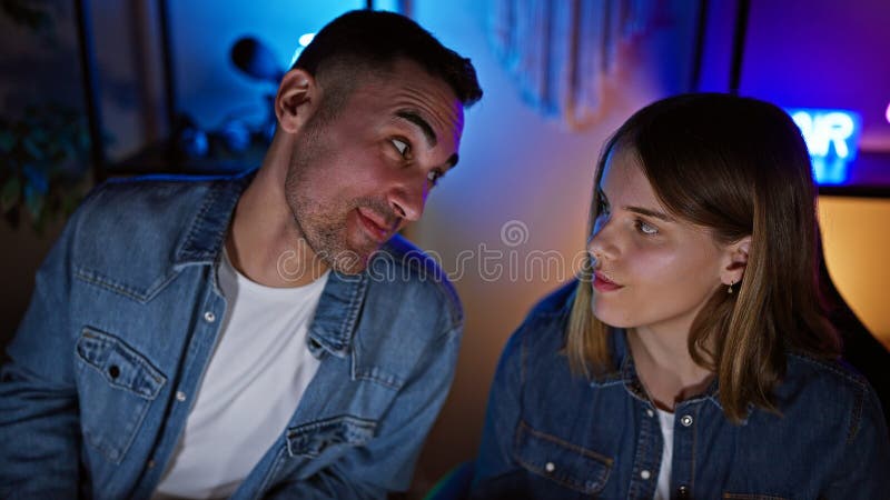 In una casa accogliente, una coppia gode di tempo libero insieme, illuminata dalle colorate luci delle sale da gioco immagini stock libere da diritti