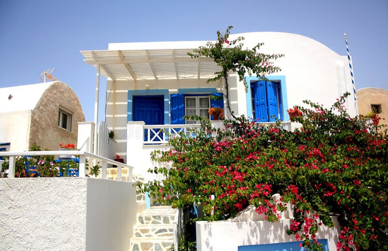 Una casa bianca con le porte e le strutture della finestra dipinte blu e cespuglio con i fiori sulla scena anteriore nell'isola d immagini stock libere da diritti Una casa bianca con le porte e le strutture della finestra dipinte blu e cespuglio con i fiori sulla scena anteriore nell'isola d immagini stock libere da diritti