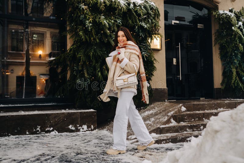 Una chica con el pelo largo en una bufanda y con un bolso blanco camina por la calle en invierno fotografía de archivo libre de regalías