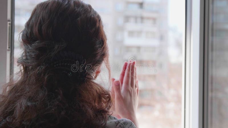 Una chica con una máscara protectora está sentada en casa con selfisolación. una niña se abalanzó sobre la ventana en apoyo a la g