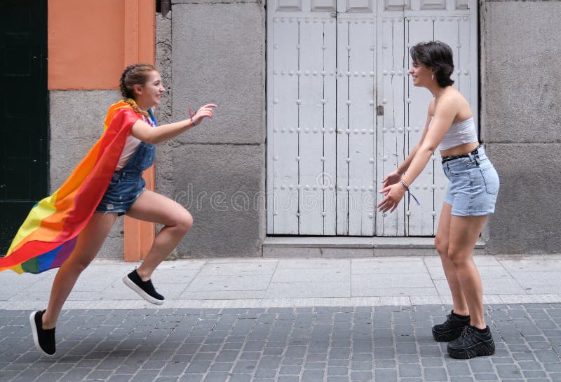 Una Chica Corriendo Para Abrazar A Su Novia Con Una Bandera De Lgbt Atada Como Un Manto Imagen