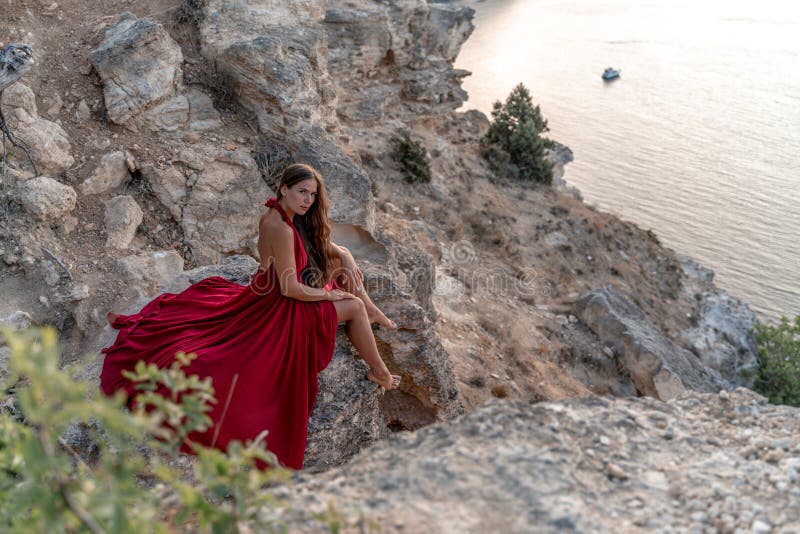 Una Muchacha Con El Pelo Suelto Vestido De Rojo Se Sobre Una Roca Sobre El Mar. Fondo Del Mar. El Concepto De Imagen de archivo - Imagen de azul,