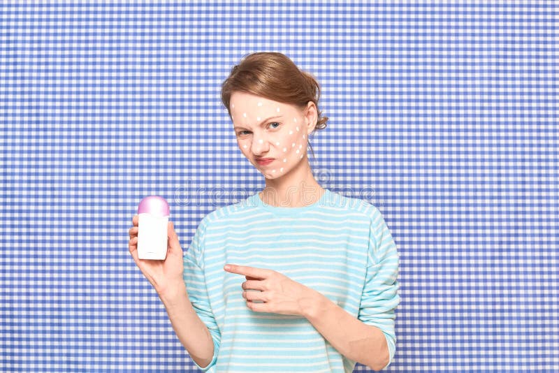 Una chica disgustada con la cara problemática de la piel apunta al desodorante