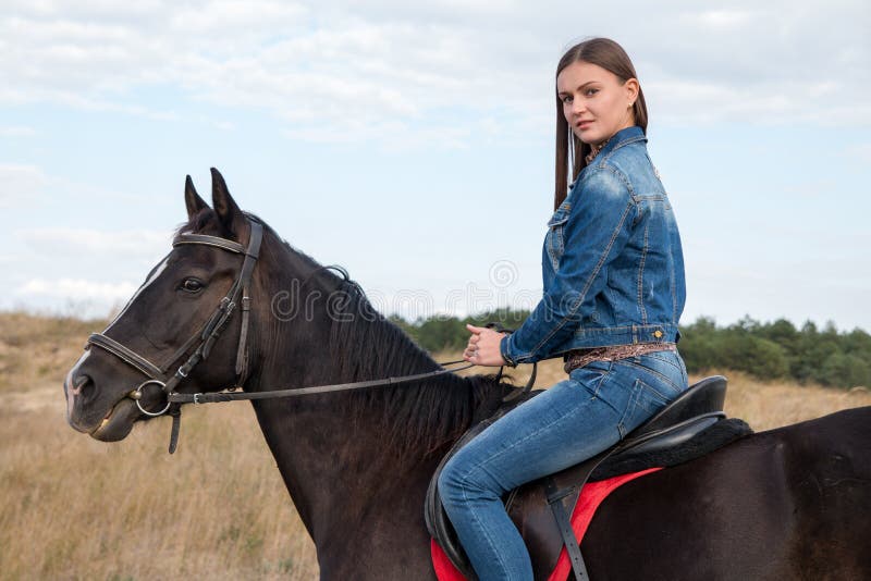 Una chica joven en un caballo oscuro imagen de archivo libre de regalías Una chica joven en un caballo oscuro imagen de archivo libre de regalías