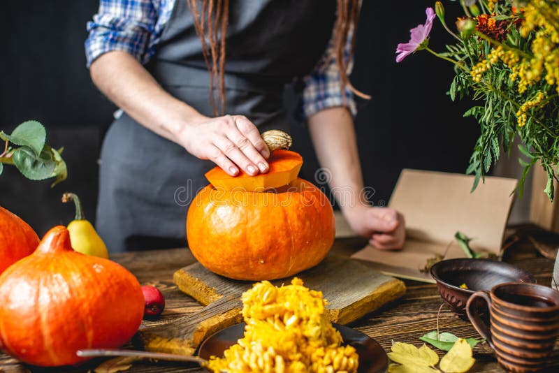 Una cocinera cocinera una calabaza naranja para cocinar con miel y canela Concepto de comida otoñal en una cocina de madera oscur fotos de archivo
