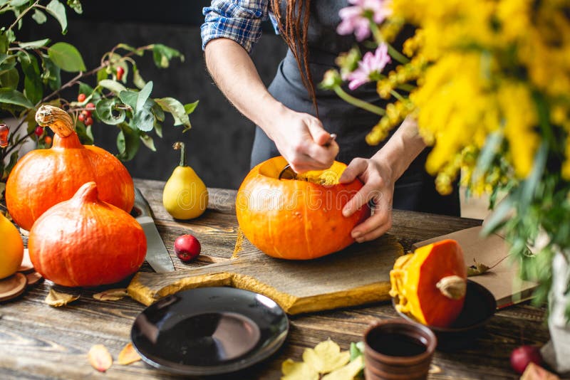 Una cocinera limpia una calabaza naranja para hacer sopa de calabaza Concepto de comida de otoño en una acogedora cocina de mader fotos de archivo