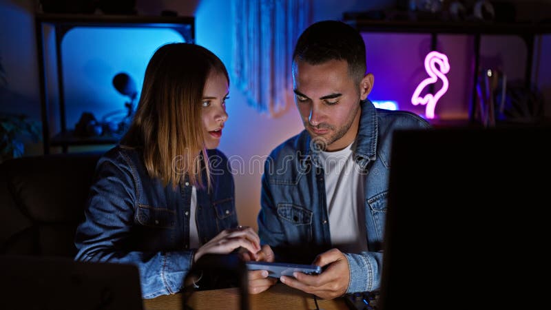Una coppia impegnata a giocare su un tablet in una stanza neonilluminata per giochi domestici di notte fotografia stock libera da diritti