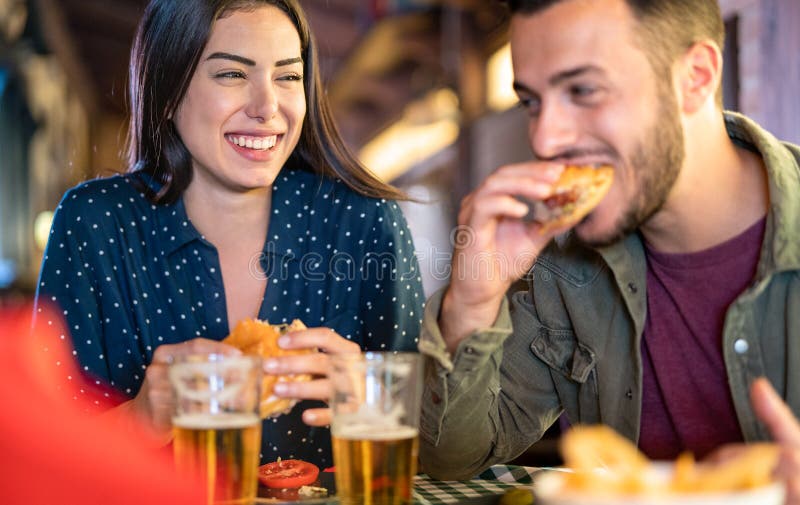 Una coppia innamorata che si diverte a mangiare hamburger al ristorante - giovani felici che si divertono nel momento del cibo al fotografia stock Una coppia innamorata che si diverte a mangiare hamburger al ristorante - giovani felici che si divertono nel momento del cibo al fotografia stock