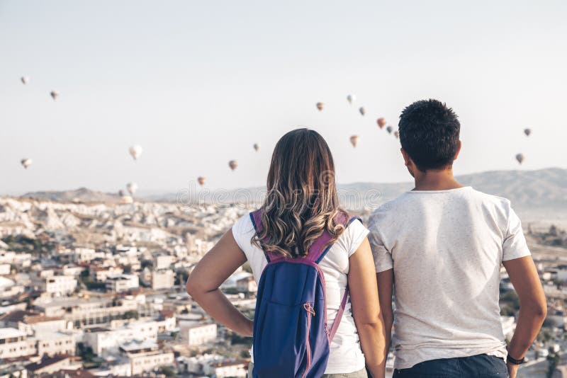 Una coppia si erge su una montagna e guarda il volo di palloncini d'aria calda nel cielo Viaggio romantico Cappadocia, Turchia fotografie stock libere da diritti Una coppia si erge su una montagna e guarda il volo di palloncini d'aria calda nel cielo Viaggio romantico Cappadocia, Turchia fotografie stock libere da diritti