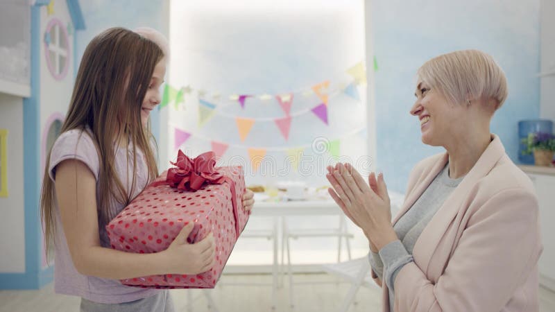 Una donna adulta regalava alla sua felice bambina un regalo di compleanno e batteva le mani di fronte alla telecamera in una stan