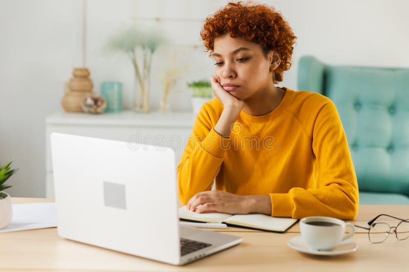 Una donna africana triste e assonnata seduta a tavola col computer portatile. Stanca una ragazza pigra al lavoro. Studente immagine stock libera da diritti