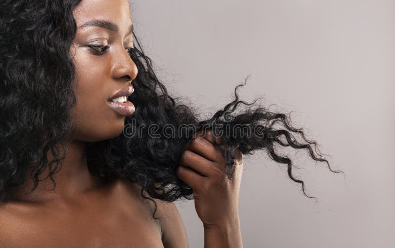 Una donna afro-americana delusa che guarda i suoi capelli asciutti e danneggiati