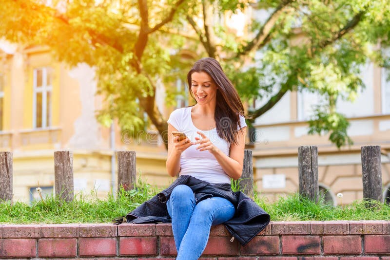 Una donna allegra in un parco facendo uso del suo Smartphone immagine stock Una donna allegra in un parco facendo uso del suo Smartphone immagine stock