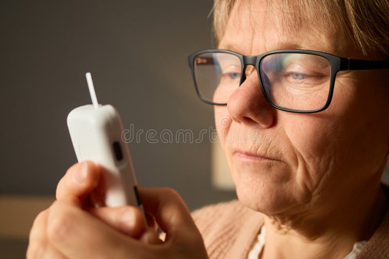 Una donna anziana esamina attentamente una lettura di glucometro che dimostra di essere concentrata sulla gestione della salute in fotografie stock