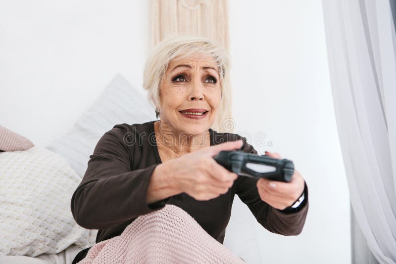 Una donna anziana sta giocando un video gioco Persona anziana e tecnologia moderna fotografie stock libere da diritti Una donna anziana sta giocando un video gioco Persona anziana e tecnologia moderna fotografie stock libere da diritti