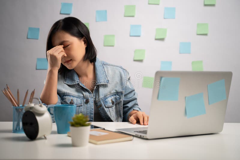 Una donna asiatica che lavora su un computer portatile è stanca e ha mal d'occhio seduto in ufficio. wfh. lavoro domestico. preven fotografie stock