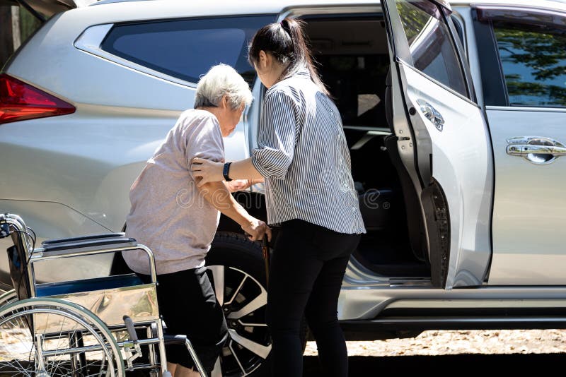 Una donna asiatica che si prende cura di lei aiuta una donna anziana disabile in sedia a rotelle a salire in macchina, aiuta le b
