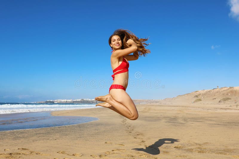 Una donna bikini sana e spensierata che salta sulla spiaggia Una ragazza felice e sorridente che salta la libertà e la felicità i immagini stock Una donna bikini sana e spensierata che salta sulla spiaggia Una ragazza felice e sorridente che salta la libertà e la felicità i immagini stock