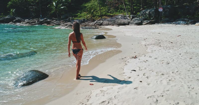 Una donna cammina lungo la spiaggia di sandy vicino a calmare le acque turchesi e la spiaggia rocciosa stock footage