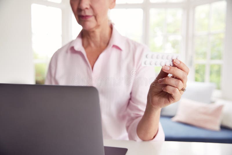 Una Donna In Casa Che Cerca Informazioni Sui Medicinali Online Usando Il Portatile fotografia stock libera da diritti Una Donna In Casa Che Cerca Informazioni Sui Medicinali Online Usando Il Portatile fotografia stock libera da diritti