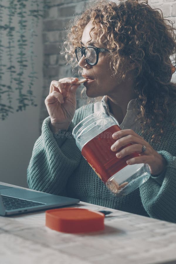 Una donna a casa che usa il portatile e mangia biscotti dalla scatola. concetto di cattiva alimentazione abitudini alimentari stil fotografie stock libere da diritti