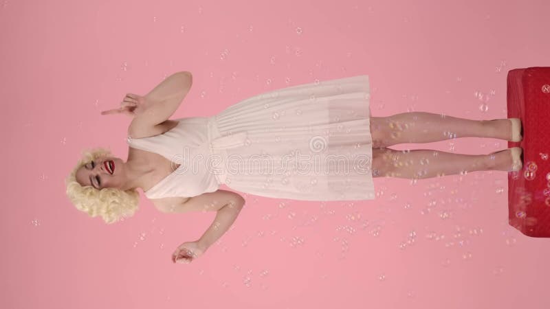 Una donna che assomiglia a marilyn monroe che dice eccitatamente wow e si diverte con bolle di sapone che le volano attorno. giova