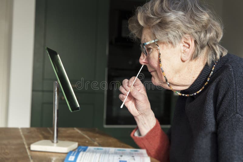 A woman looing in a mirror taking a covid-19 home testing nasal swab. A woman looing in a mirror taking a covid-19 home testing nasal swab.