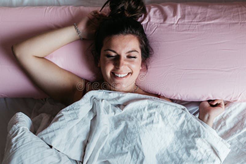 Laughing woman tries to fall asleep lying down on the bed. Happy smiling and beautiful long hair. Lifestyle concept. Laughing woman tries to fall asleep lying down on the bed. Happy smiling and beautiful long hair. Lifestyle concept.