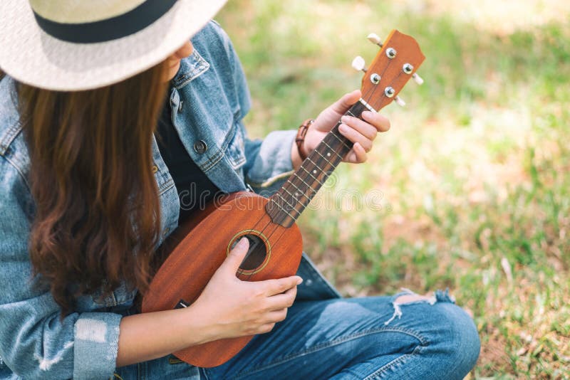 Una donna che si siede e che gioca ukulele fotografia stock libera da diritti Una donna che si siede e che gioca ukulele fotografia stock libera da diritti