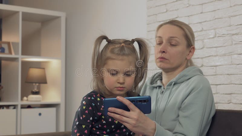 Una donna con una bambina seduta sul divano a casa che guarda lo schermo dello smartphone e ride
