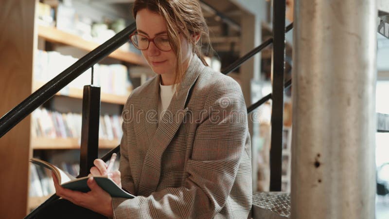 Una donna con una giacca di plastica siede sulle scale in una libreria stock footage