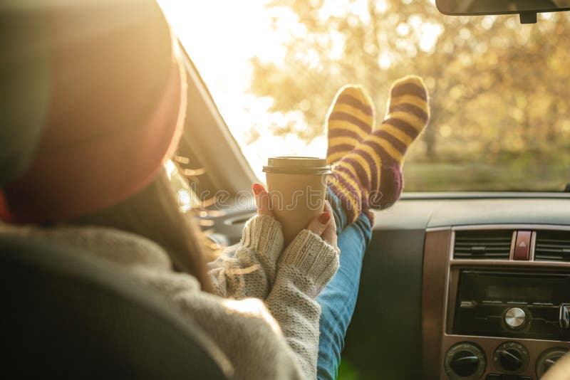 Woman in a car in warm woolen socks yellow is holding a Cup of coffee in hands at sunset. Cozy autumn weekend trip. The concept of freedom of travel. Woman in a car in warm woolen socks yellow is holding a Cup of coffee in hands at sunset. Cozy autumn weekend trip. The concept of freedom of travel