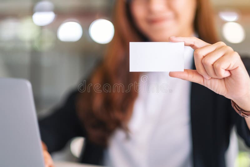 Una donna d'affari asiatica che tiene in mano e mostra biglietti da visita vuoti mentre utilizza un computer portatile fotografia stock Una donna d'affari asiatica che tiene in mano e mostra biglietti da visita vuoti mentre utilizza un computer portatile fotografia stock
