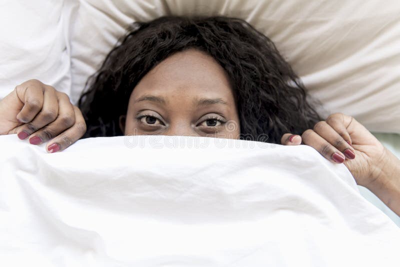 Una donna di colore impaurita sotto la coperta del letto immagini stock libere da diritti