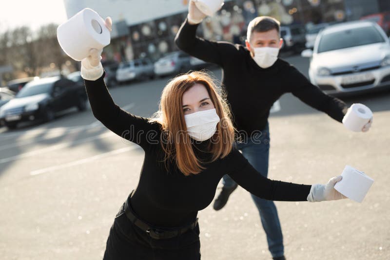 Una donna e un uomo con una maschera anti-coronavirus tengono grandi rotoli di carta igienica in una strada della città e indulgon