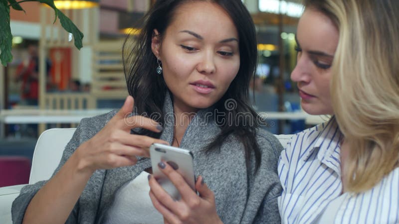 Una donna felice che fa shopping in asia usa uno smartphone con un amico biondo in un centro commerciale