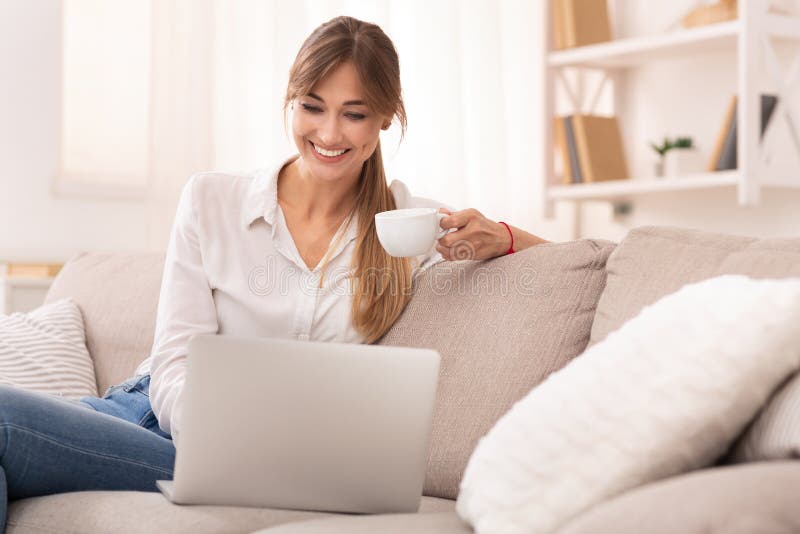 Happy Lady Watching Film On Laptop Drinking Coffee Relaxing On Couch At Home. Movie Weekend. Selective Focus. Happy Lady Watching Film On Laptop Drinking Coffee Relaxing On Couch At Home. Movie Weekend. Selective Focus