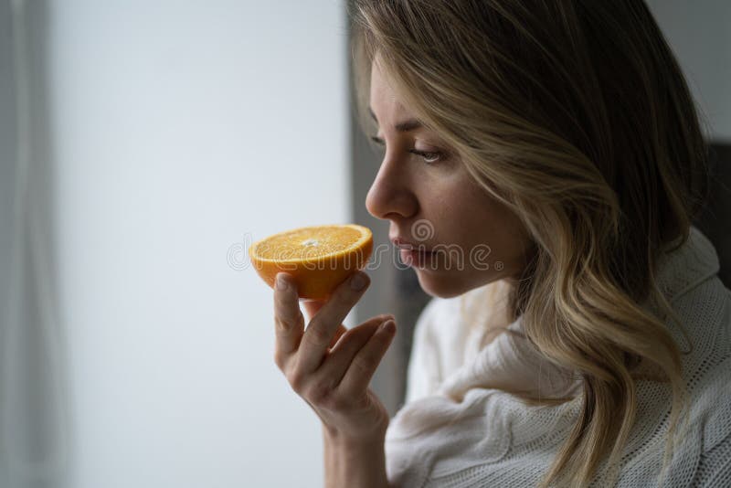 Una donna malata che cerca di sentire l'odore di mezza arancia fresca ha il sintomo della perdita di gusto di covid19