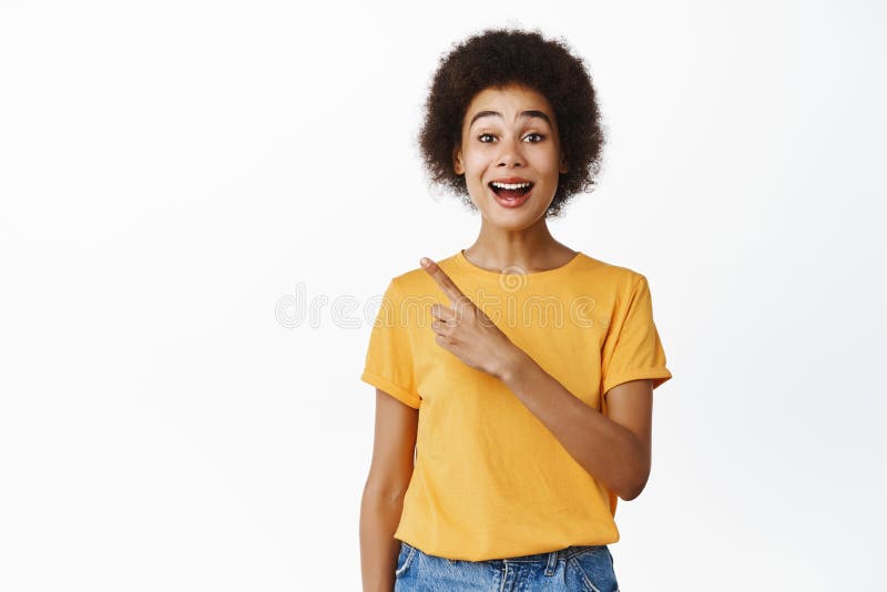 Una donna nera entusiasta che punta il dito verso l'angolo in alto a sinistra e sorridente per l'offerta promozionale sorpresa dal fotografie stock libere da diritti