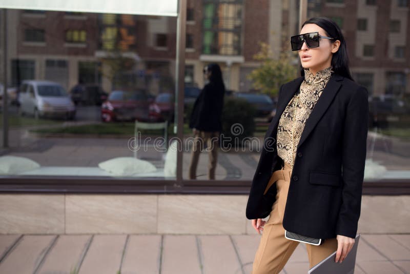 Una donna in occhiali e un vestito da donna tiene in mano una cartella Stampa di leopardo immagine stock Una donna in occhiali e un vestito da donna tiene in mano una cartella Stampa di leopardo immagine stock