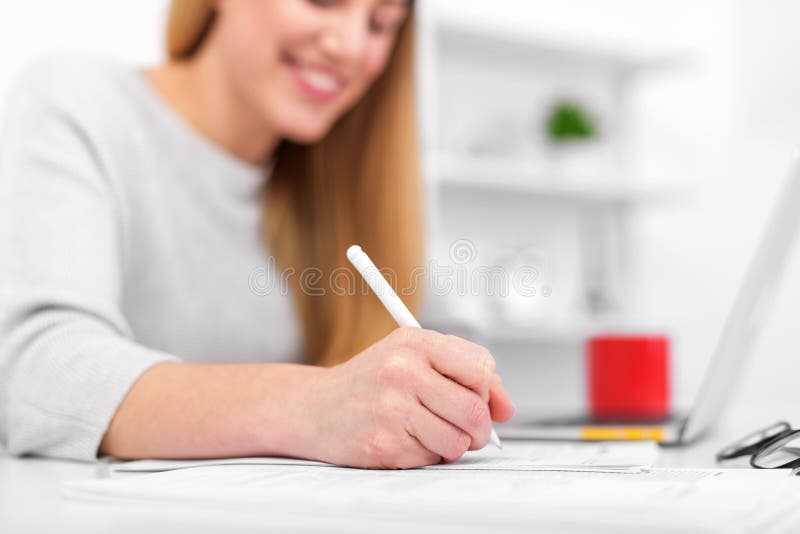 Una donna scrive mentre si siede ad una tavola in un ufficio o in un'aula La ragazza compila i documenti nel luogo di lavoro face immagini stock libere da diritti Una donna scrive mentre si siede ad una tavola in un ufficio o in un'aula La ragazza compila i documenti nel luogo di lavoro face immagini stock libere da diritti
