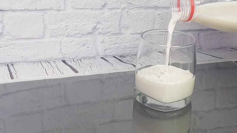 Una donna spruzza un bicchiere di latte limpido contro un muro di mattoni bianco. l'importanza dei prodotti lattiero-caseari quoti