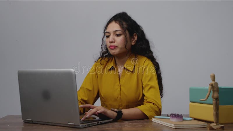 Una donna sudasiatica concentrata che scrive sul suo portatile e poi guarda il suo orologio per controllare l'ora video d archivio