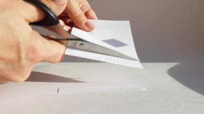 La mano di una donna taglia un foglio di carta bianca con le